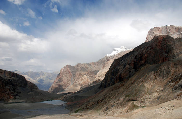 Epic landscape of rugged mountains and lake with powdering white clouds in a blue sky