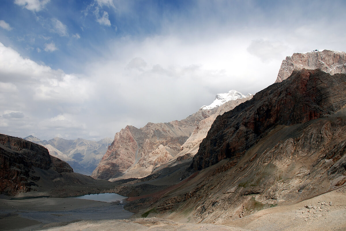 Epic landscape of rugged mountains and lake with powdering white clouds in a blue sky