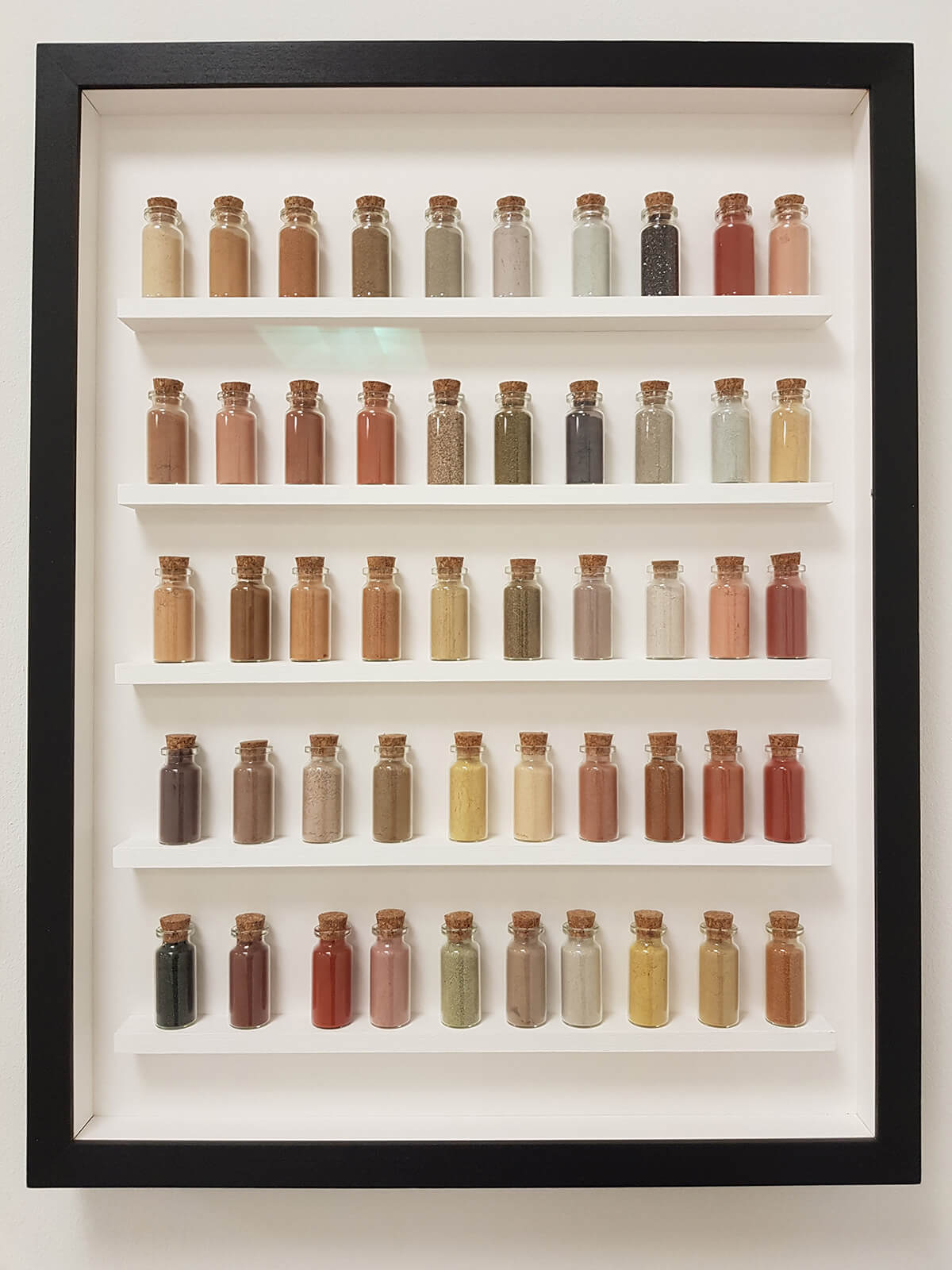 Rows of small glass bottles filled with different coloured earth and arranged like a painting in a frame