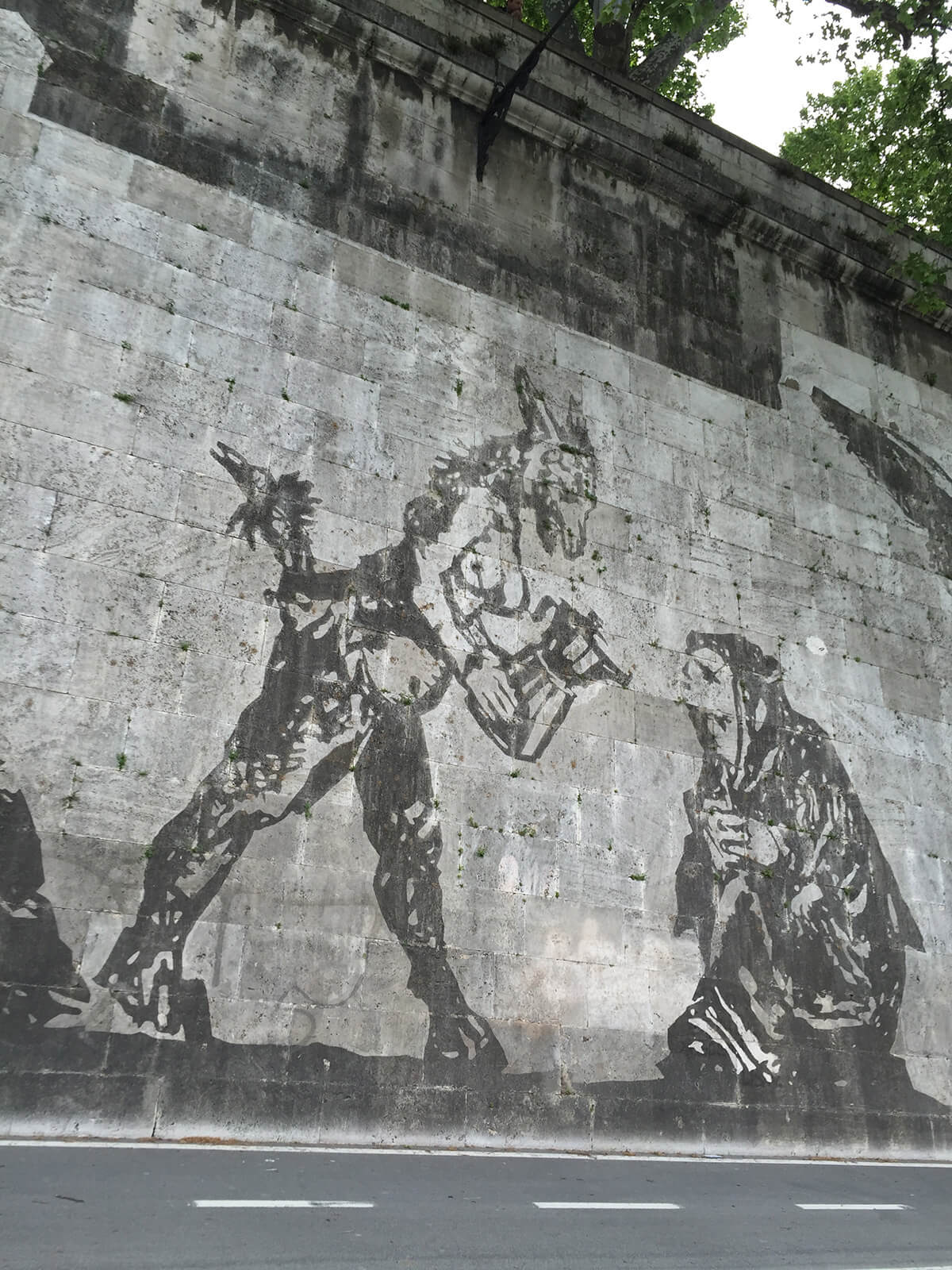 Stencil type public art illustrations on a wall of a kneeling beggar and a half animal half human creature