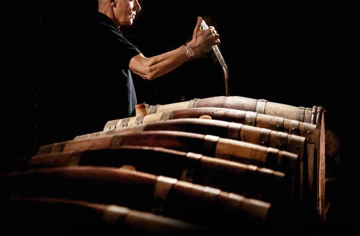 Man testing wine from a line of oak barrels