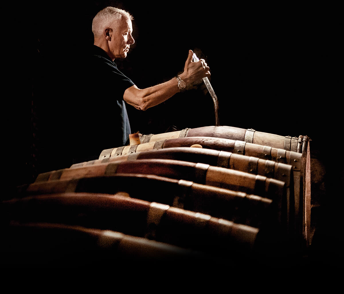 Man testing wine from a line of oak barrels
