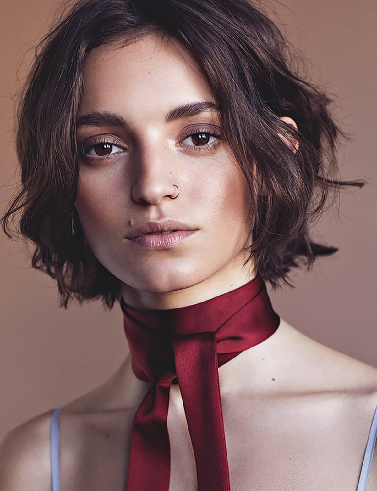 Portrait of a young woman with short brown hair and a red ribbon tied around her neck