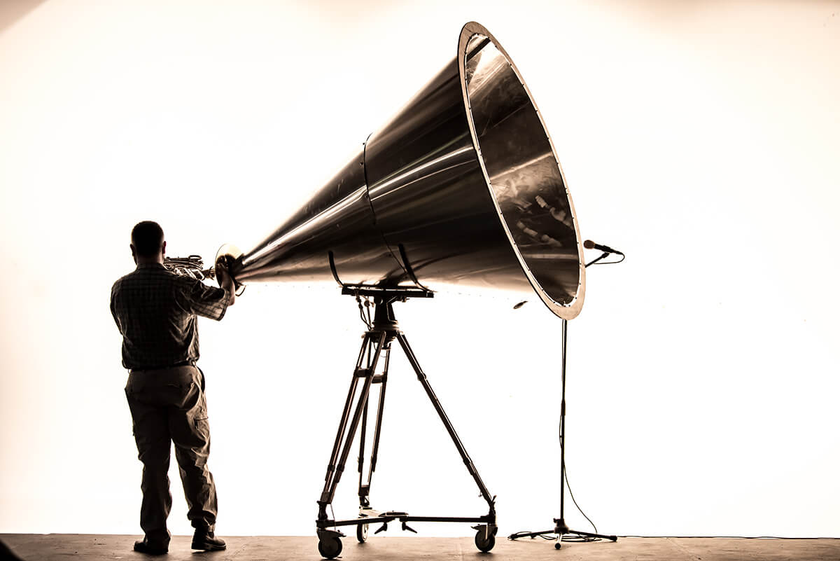 Photograph of man with large metal horn positioned on a tripod