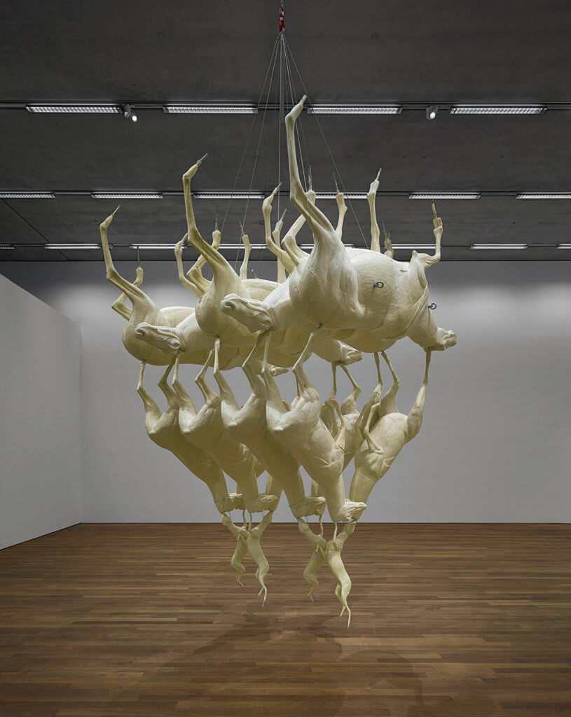 Sculpture of foxes piled on top of each other in a triangle, displayed in a gallery space
