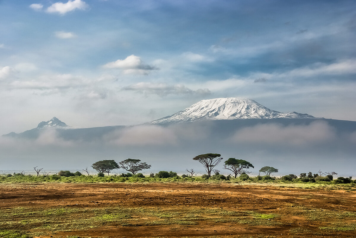 The snow-capped peak of Mount Kilimanjaro covered partially by clouds with plains in front