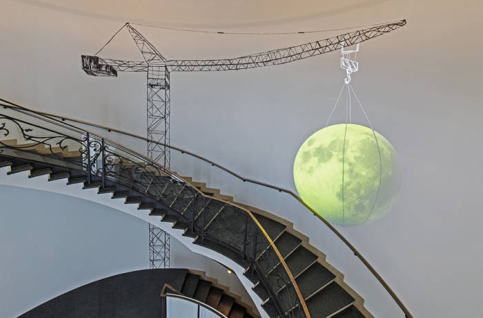 Installation set up around a staircase of a crane holding a glowing yellow planet