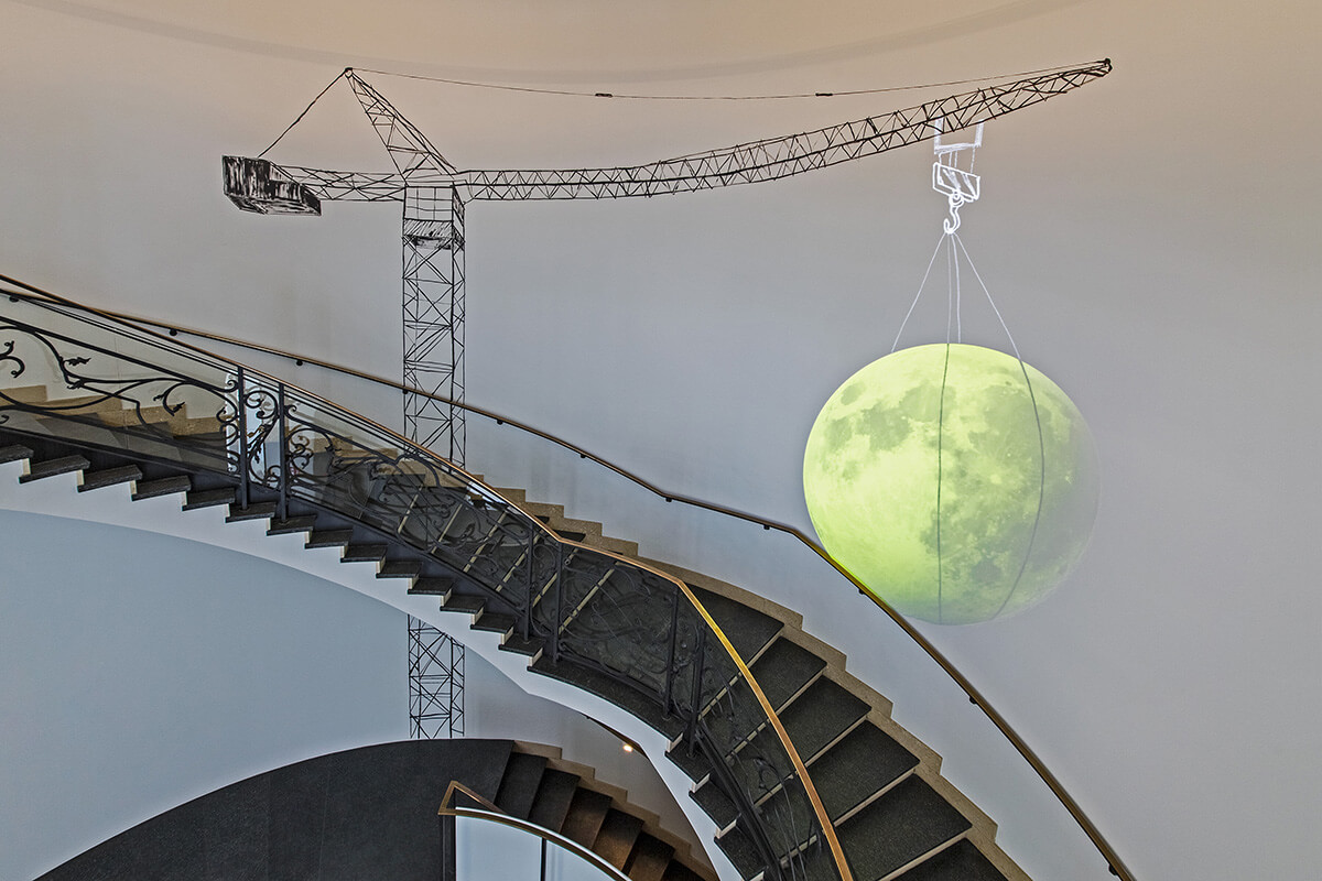 Installation set up around a staircase of a crane holding a glowing yellow planet