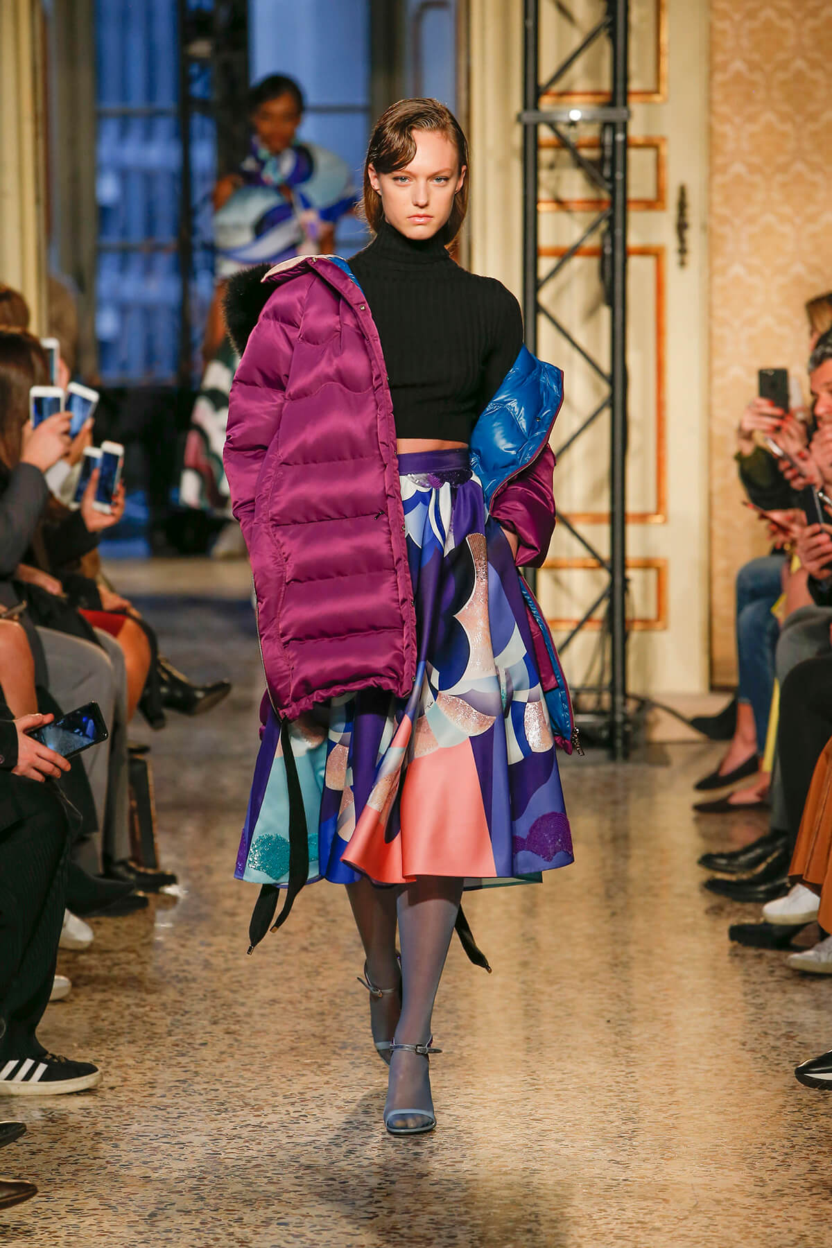 Model on catwalk wearing a purple puffer jacket and colourful skirt