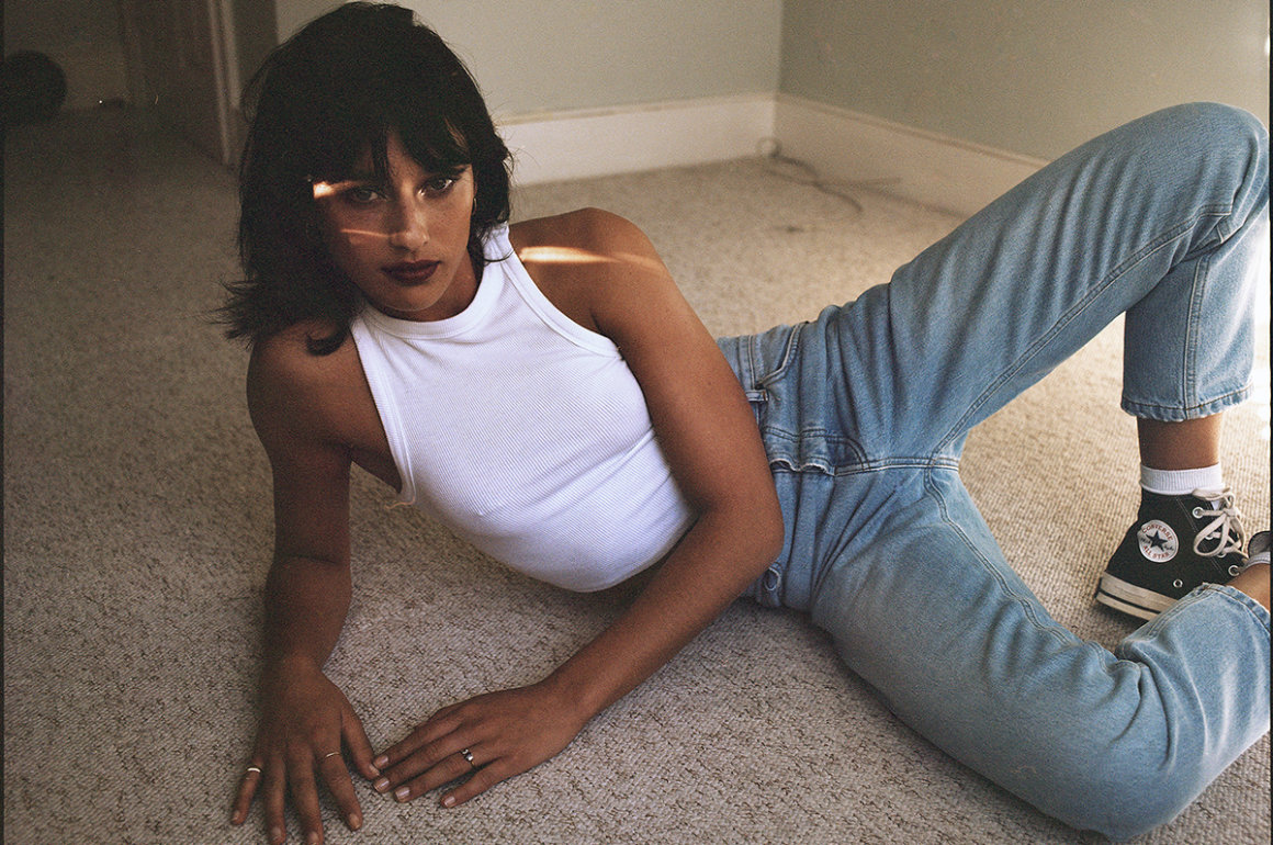 Young woman wearing jeans and white top poses lying on the ground