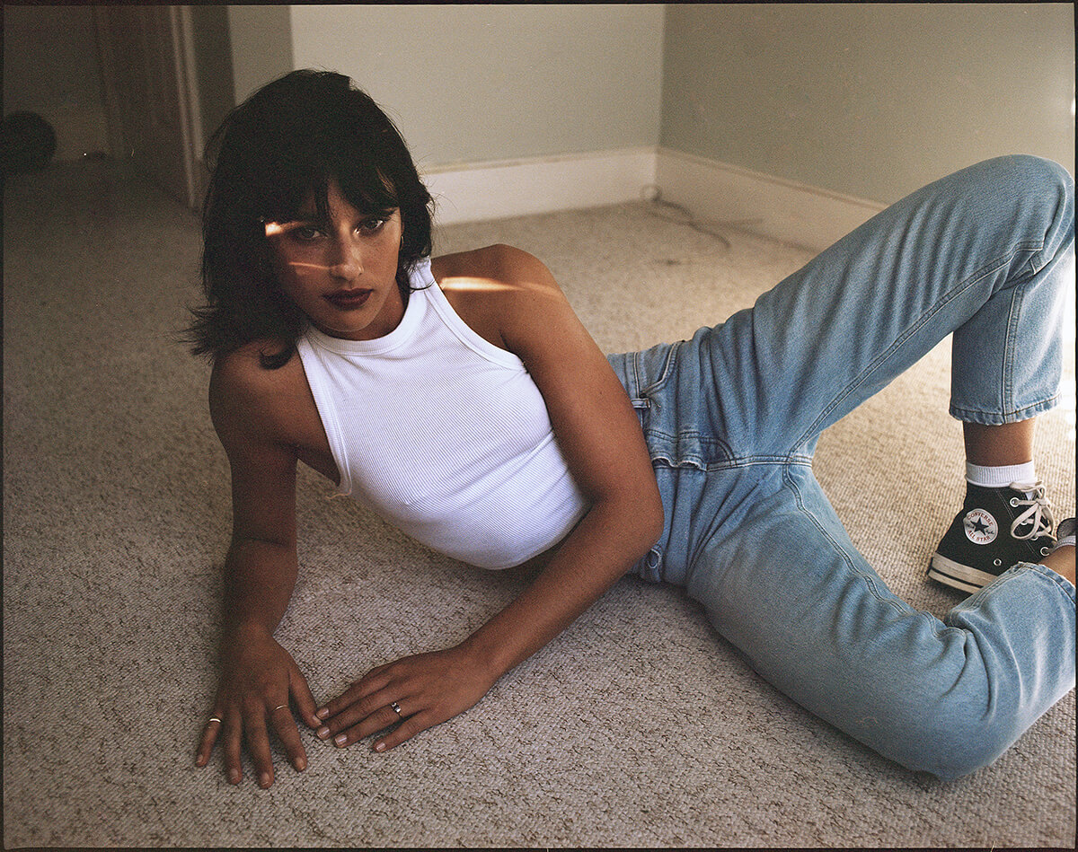 Young woman wearing jeans and white top poses lying on the ground