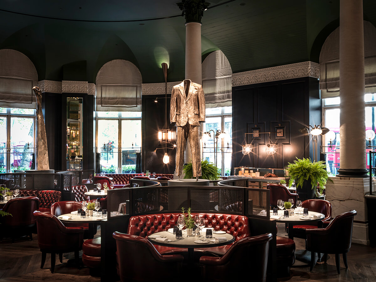 Luxury restaurant interiors with a sculpture of a man in a suit, dark green walls and plush red sofa seating