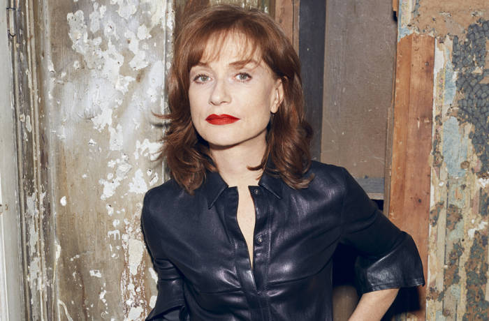 Actress Isabelle Huppert poses in front of wall in blue shirt and red lipstick