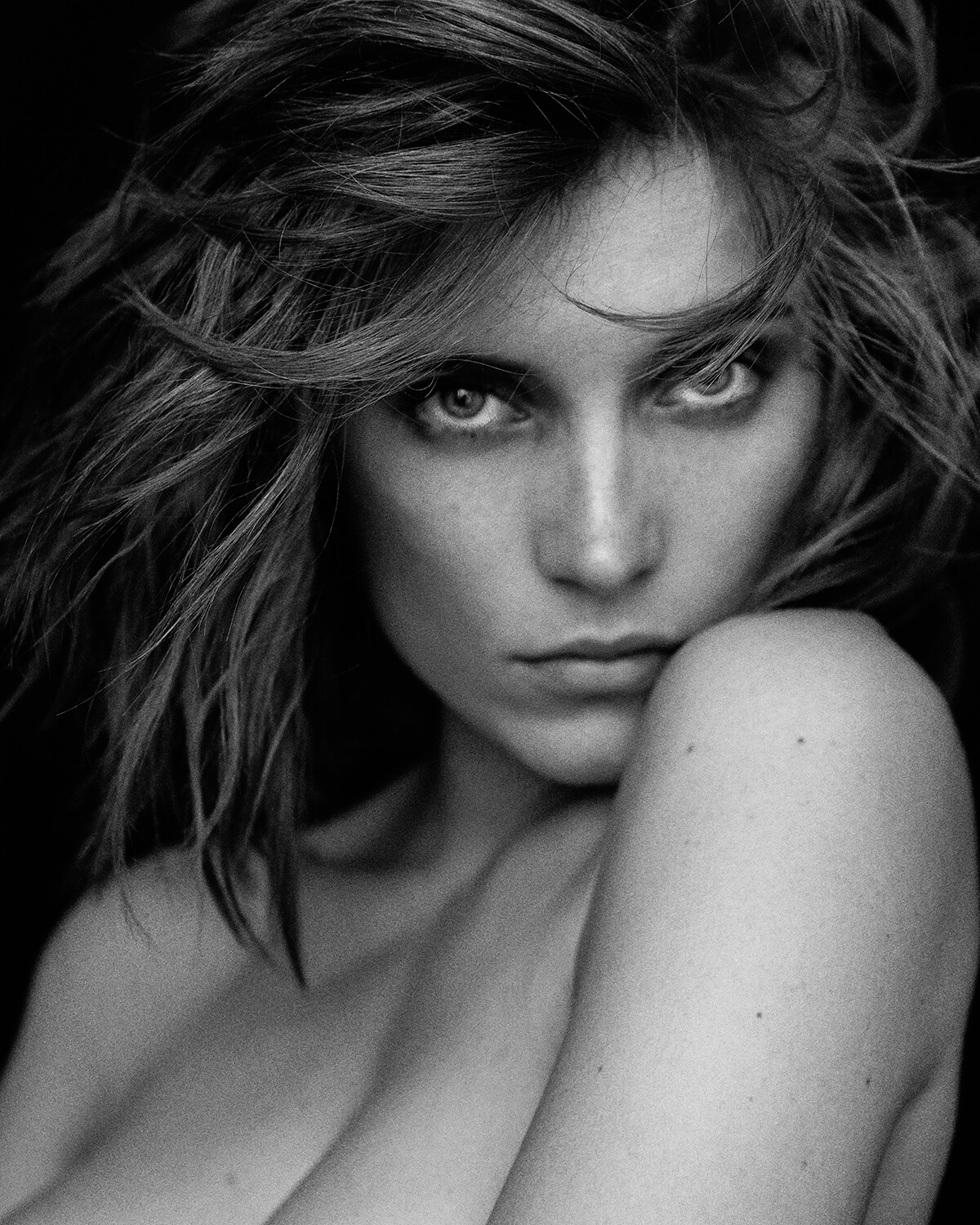 Black and white headshot of a topless woman with brown hair and natural make-up