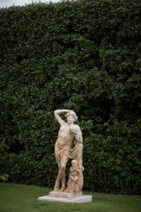 Grand garden with stone statue of a person leaning one hand on his head in front of a hedge