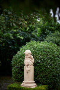 A statue of an elf sitting on top of a column in a smart stately garden