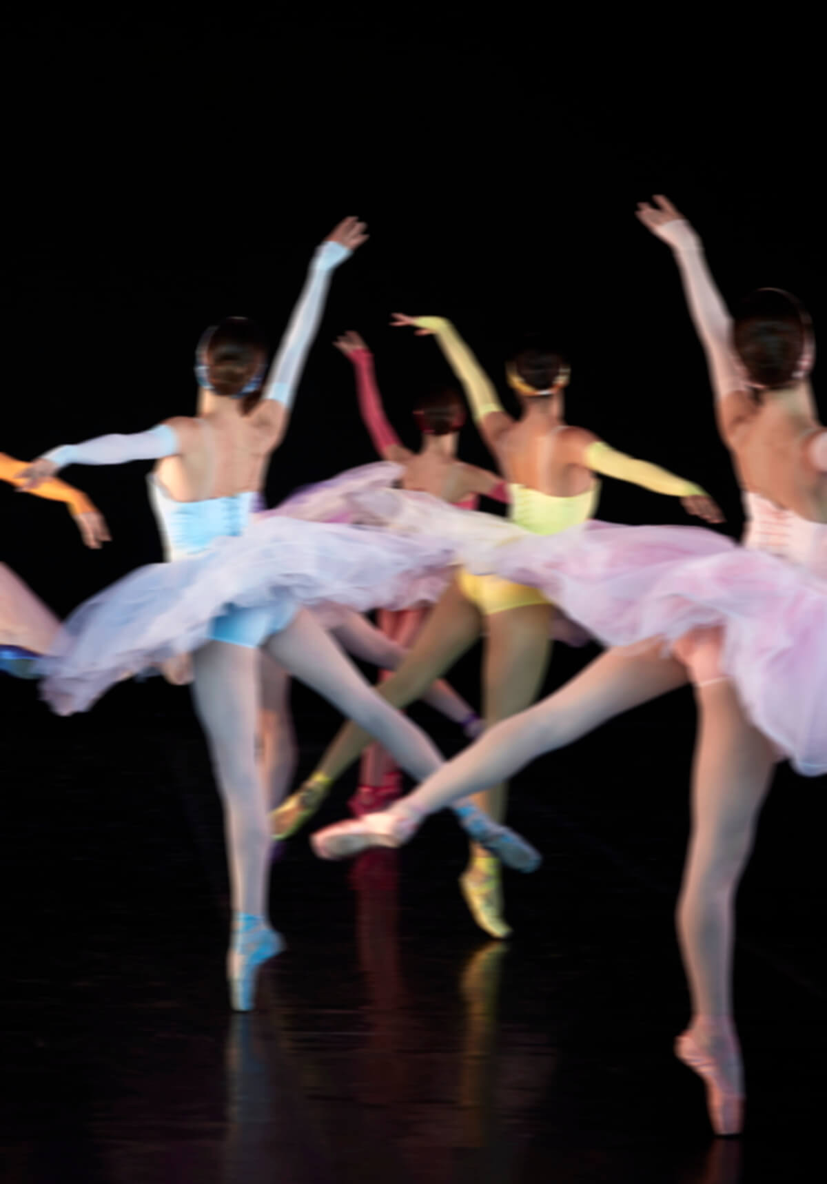 Ballet dancers in motion, performing against a backdrop in pastel clothing