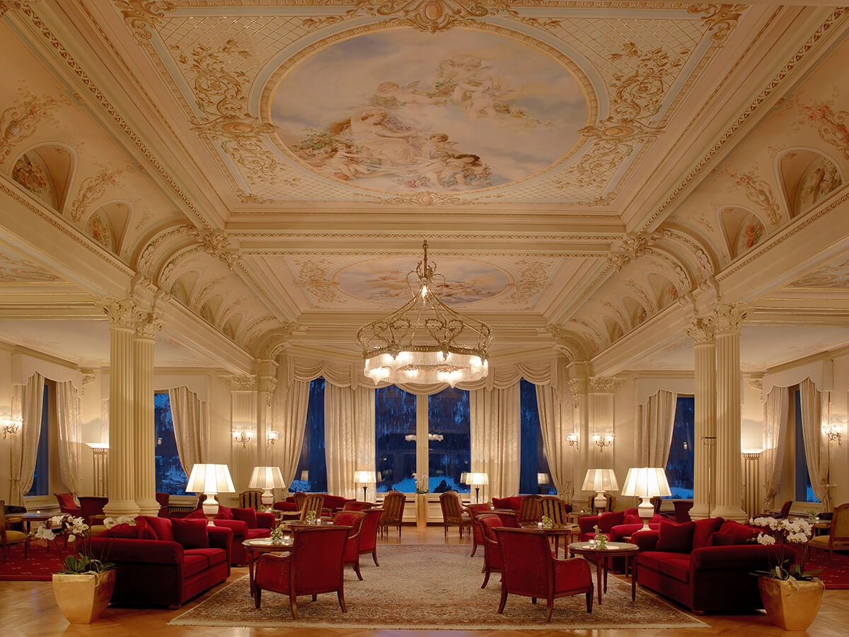 A large grand lounge with artworks on the ceiling and plush red armchairs