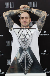 tattoo artist Maxime Büchi standing in front of a wall marked with Hublot logos