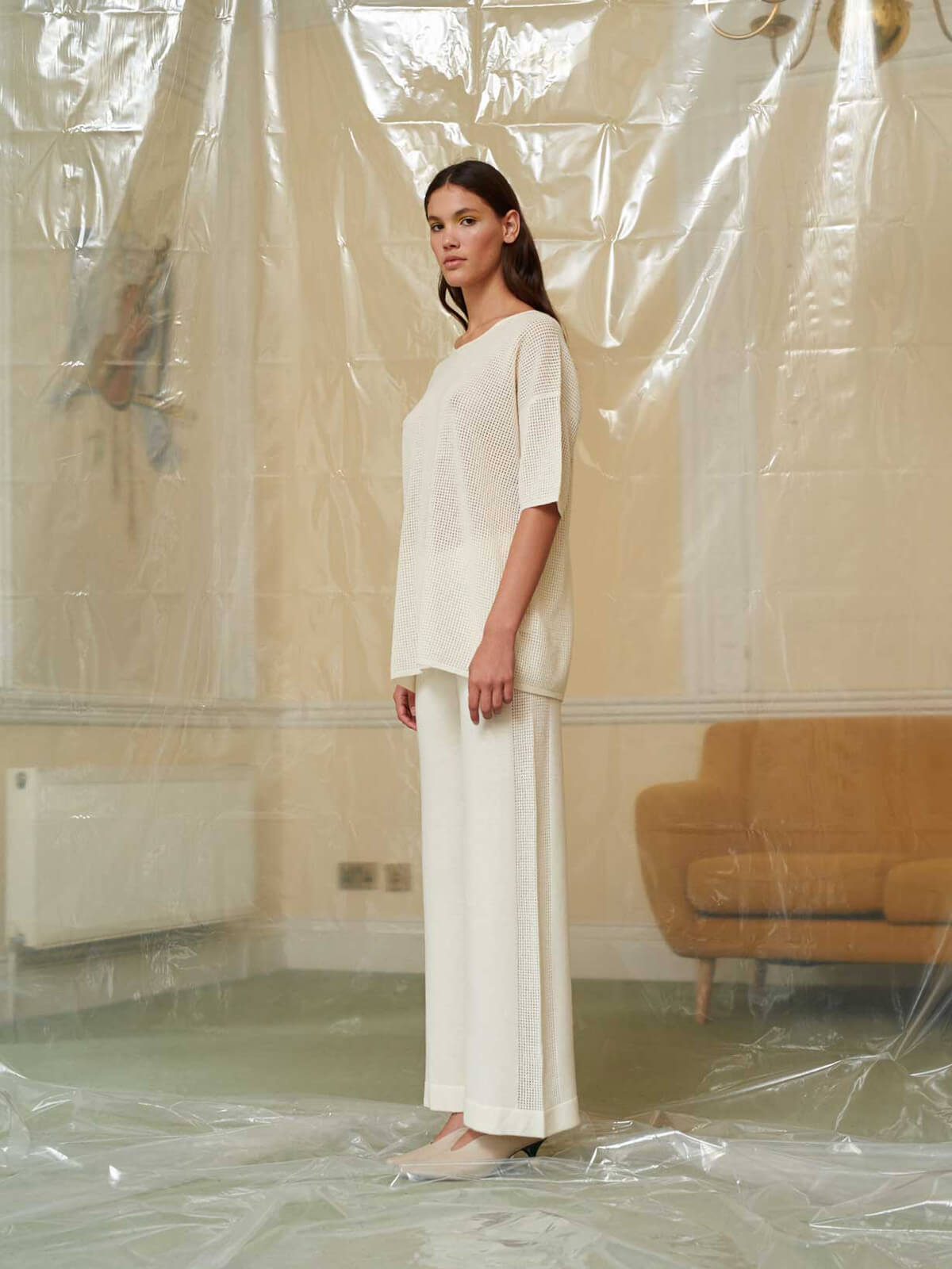 Model poses in studio setting wearing a white t-shirt and white trousers