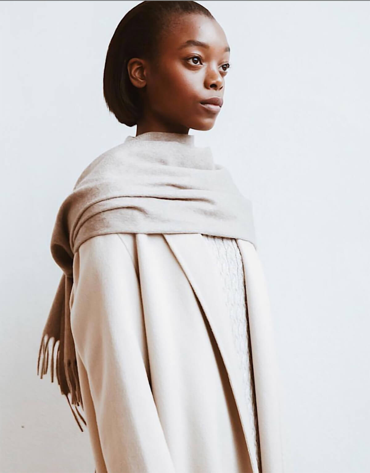 Female model poses in white scarf and coat looking into the distance