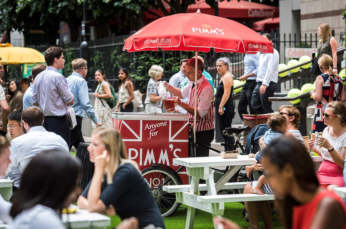 Pimms being served in a london garden from a trolley with a red umbrella