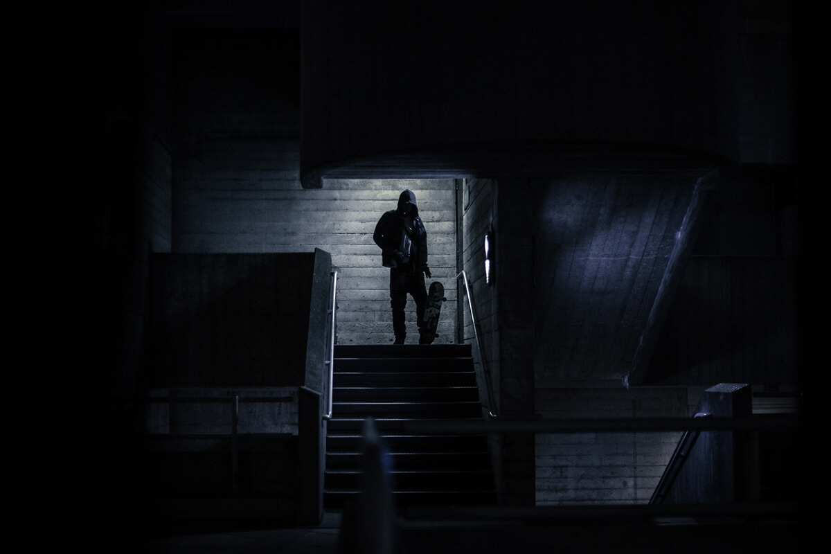 Man wearing a hoody stands at the top of concrete steps with his skateboard