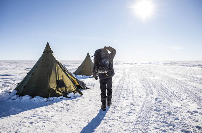 Explorer walking past base camp on a snowy landscape