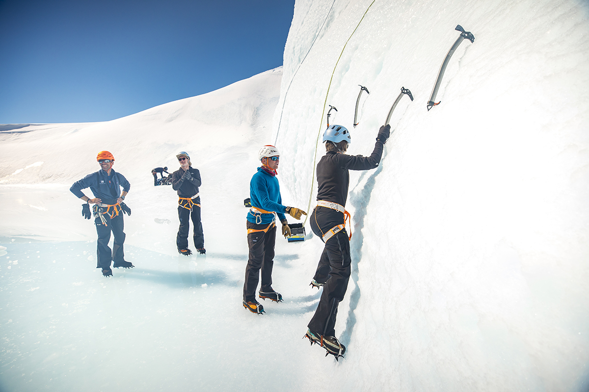 Explorers climbing up an ice wall with picks and helmets