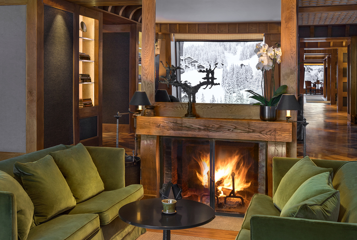Luxurious sitting room with green velvet sofas, log fire and snowy landscape through the window