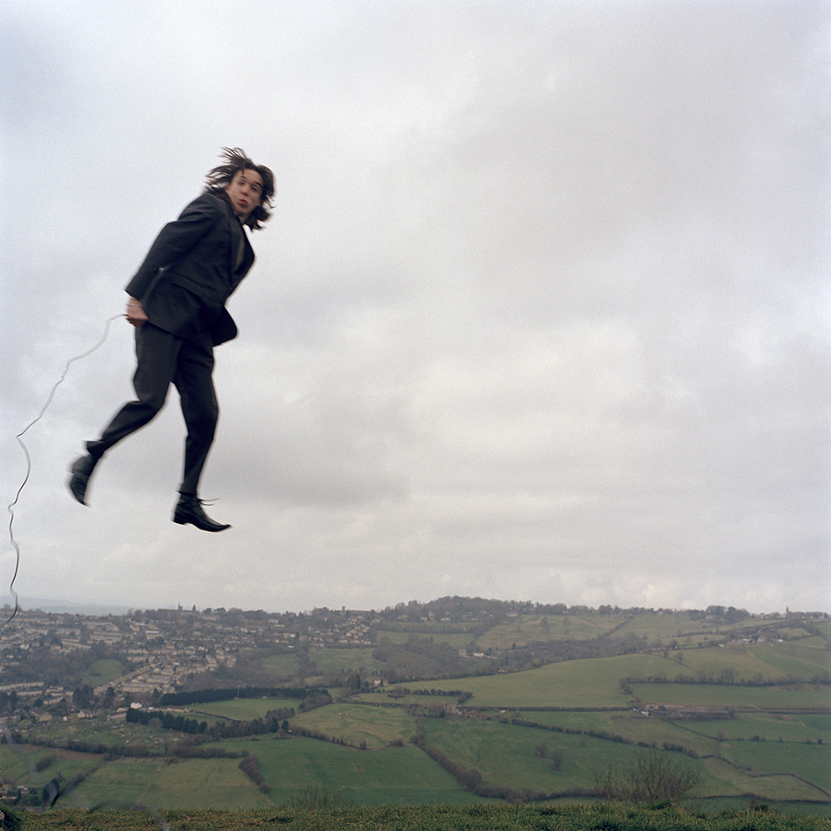 Performance artist Tom pope pictured floating in the air above a rural landscape