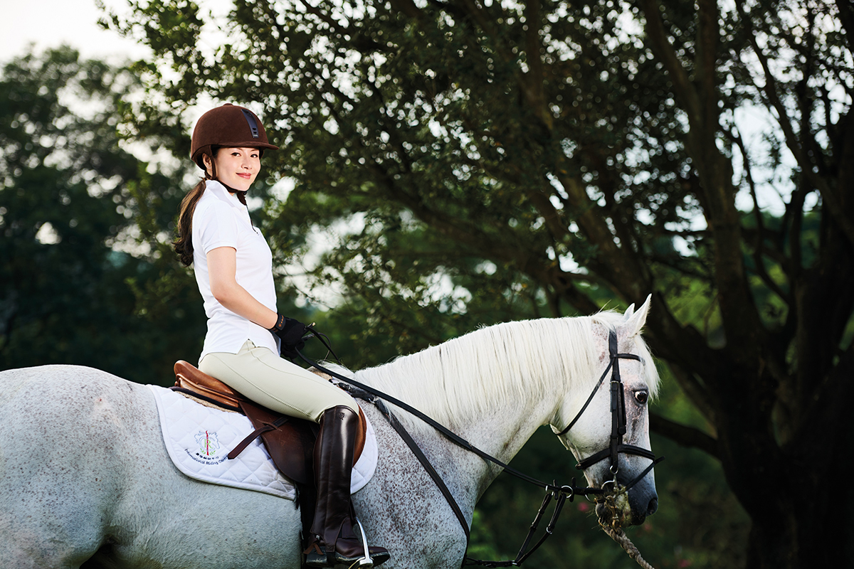 Woman riding a white horse against a leafy background