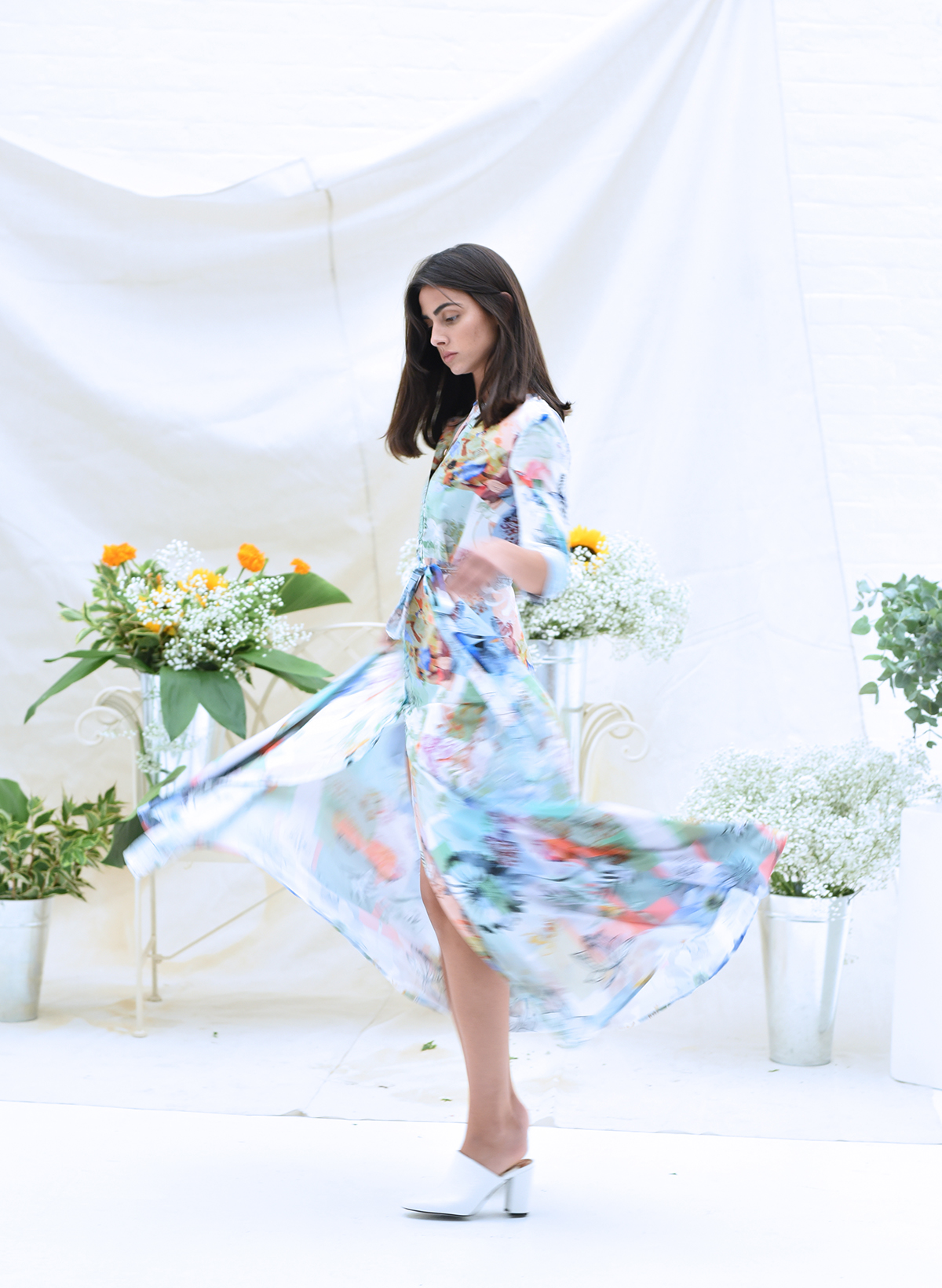 Model spins in a floral print dress with bouquets of flowers behind her