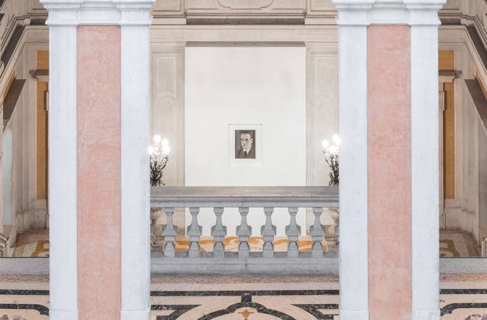 Installation shot of a Luc Tuymans exhibition with a small painting between two columns at the top of stairs