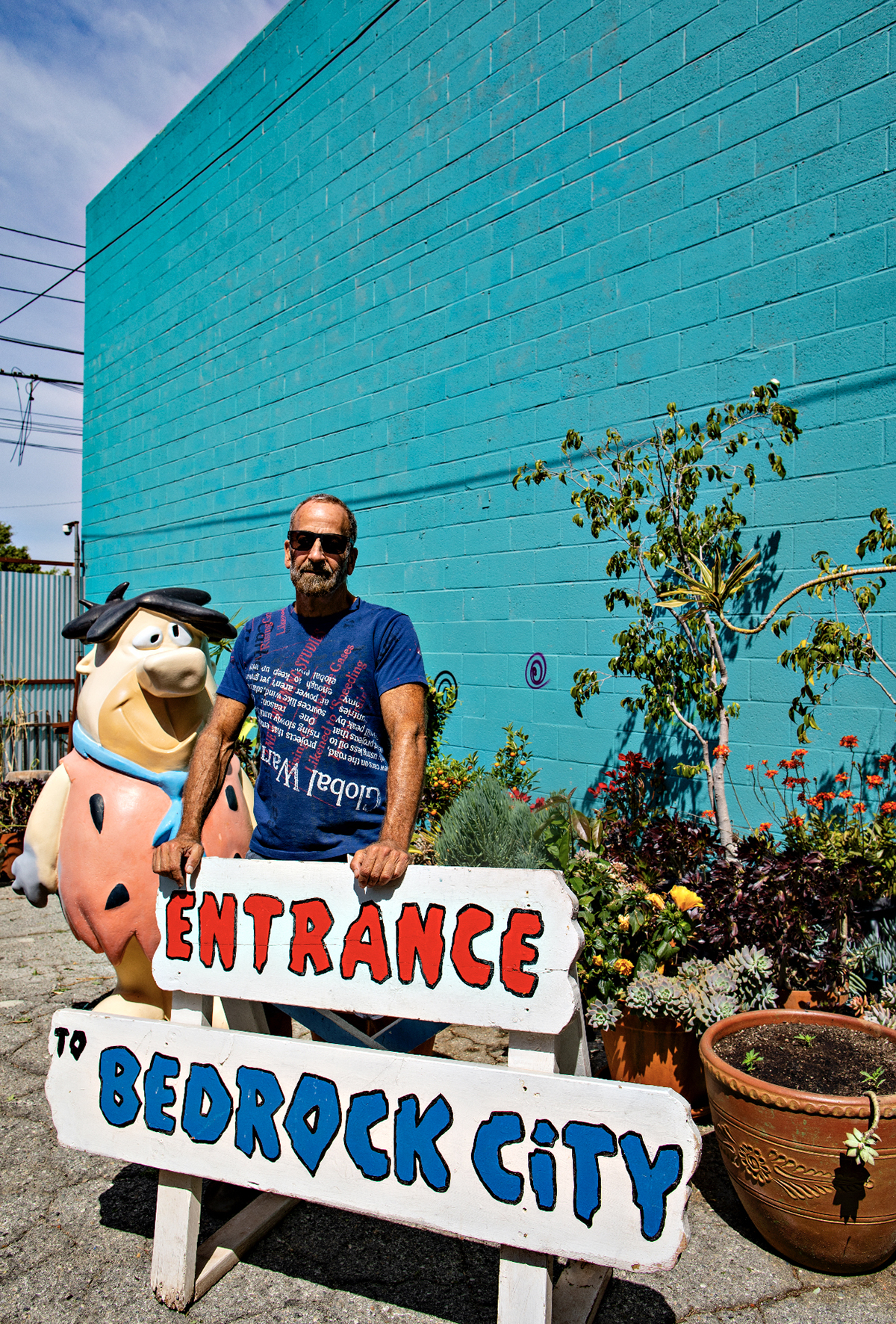 Artist Kenny Scharf standing by an entrance sign to bedrock city