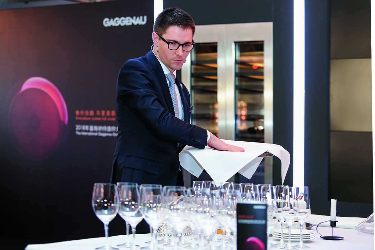 A sommelier in the act of pouring wine into a table of glasses