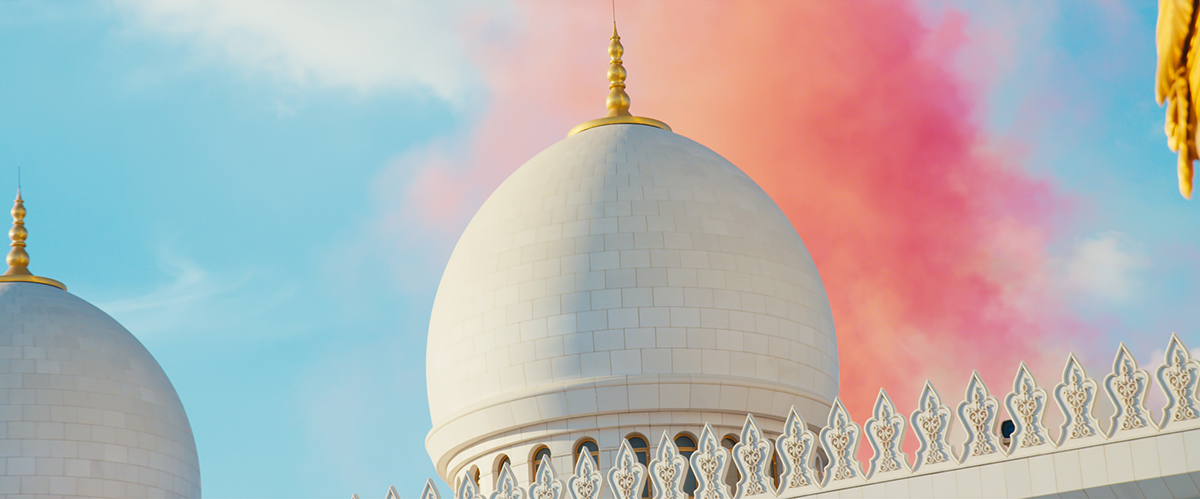 Image of a white dome with a golden spire and pink smoke in the sky behind