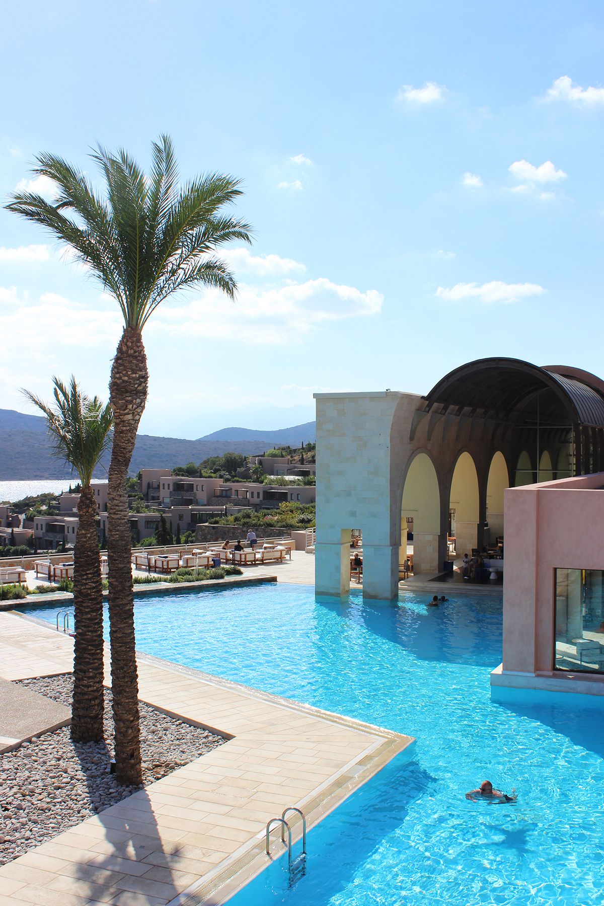 A grand luxury swimming pool area with arched building and palm trees