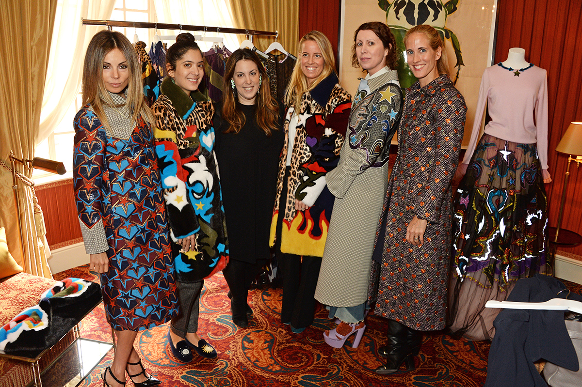 Women pose backstage in front of a rail of clothing