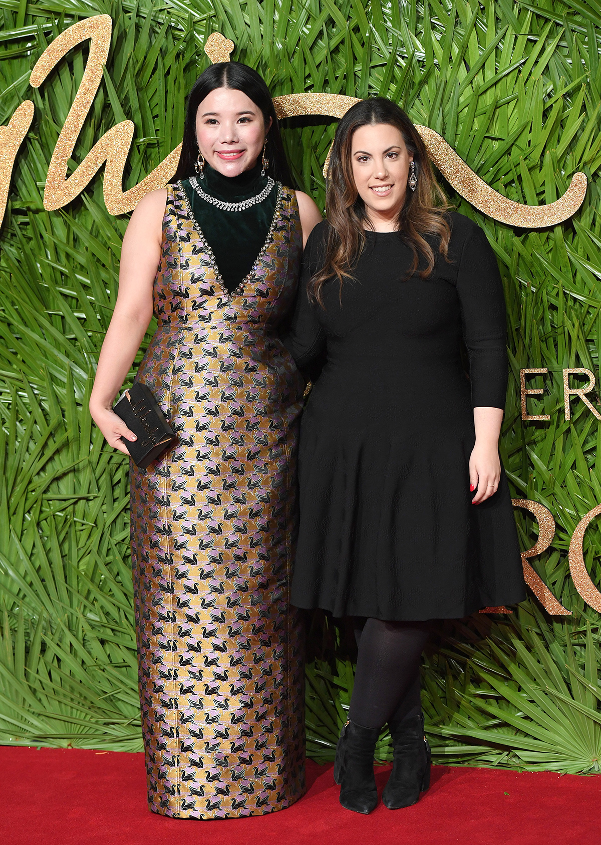 Two women posing in front of a green wall at an exclusive event