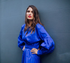 Portrait of Marine Tanguy wearing a blue dress standing against a grey blue wall