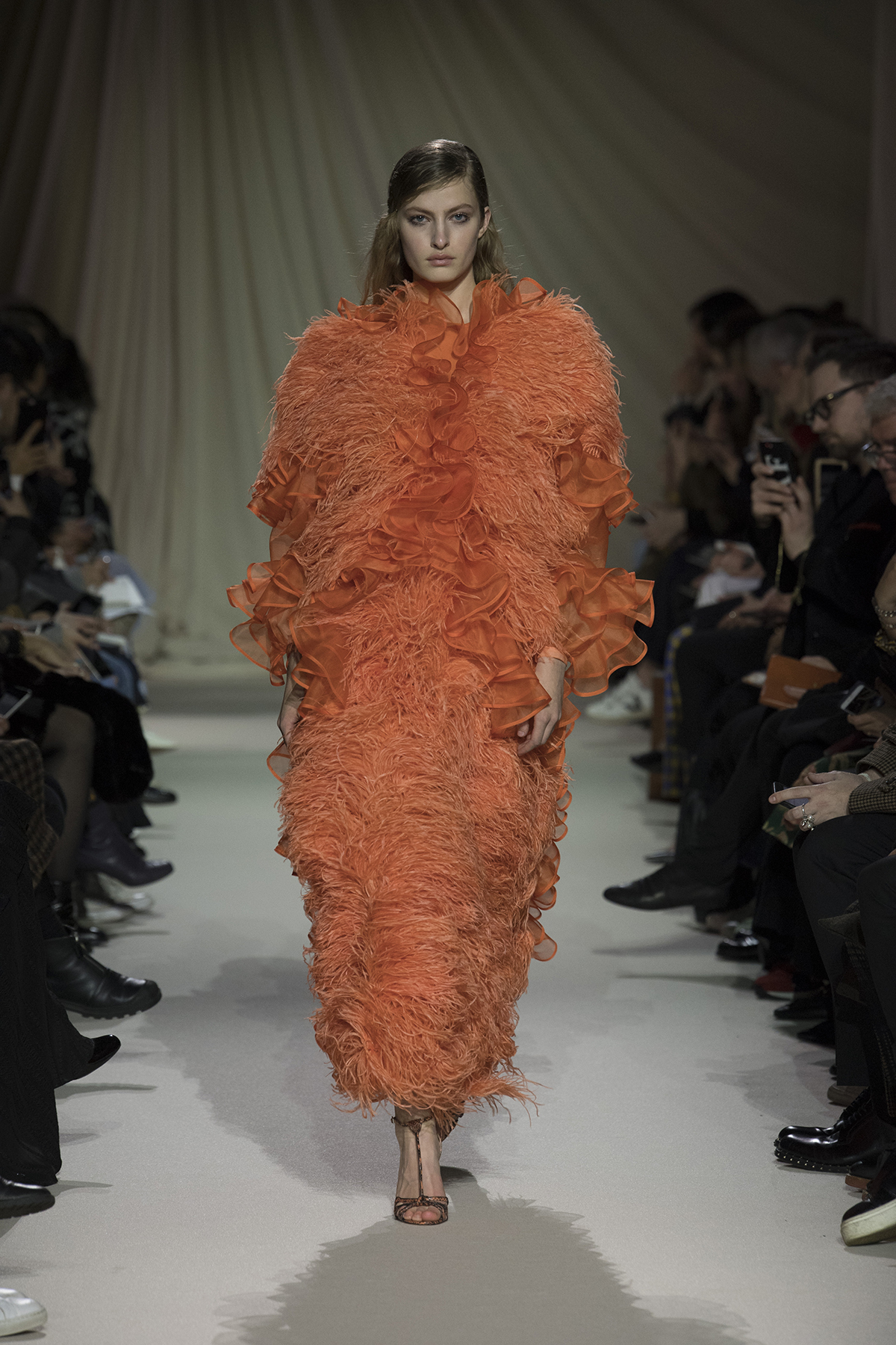 Model on catwalk wearing large orange coat