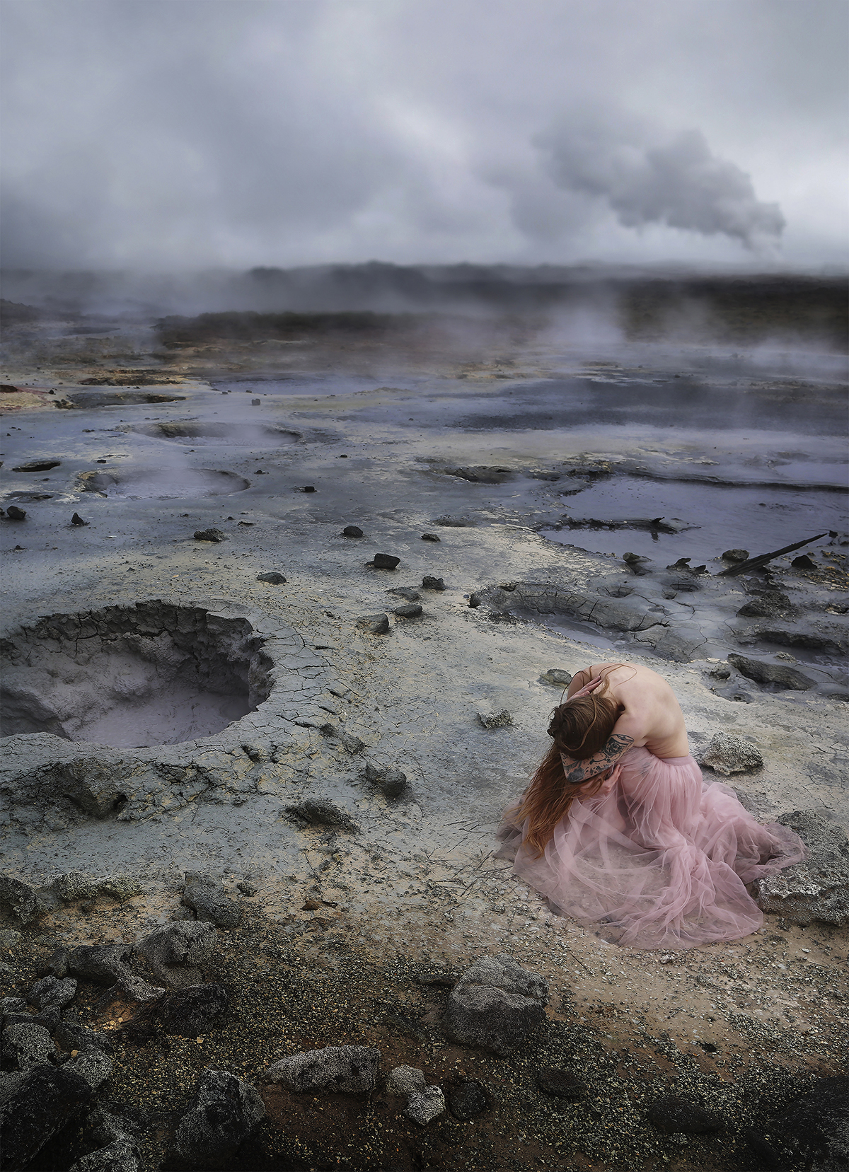 A woman crouched over in a pink skirt on a volcanic landscape