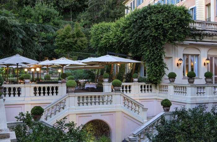 Grand terrace of a pink mansion house with umbrellas and lots of greenery