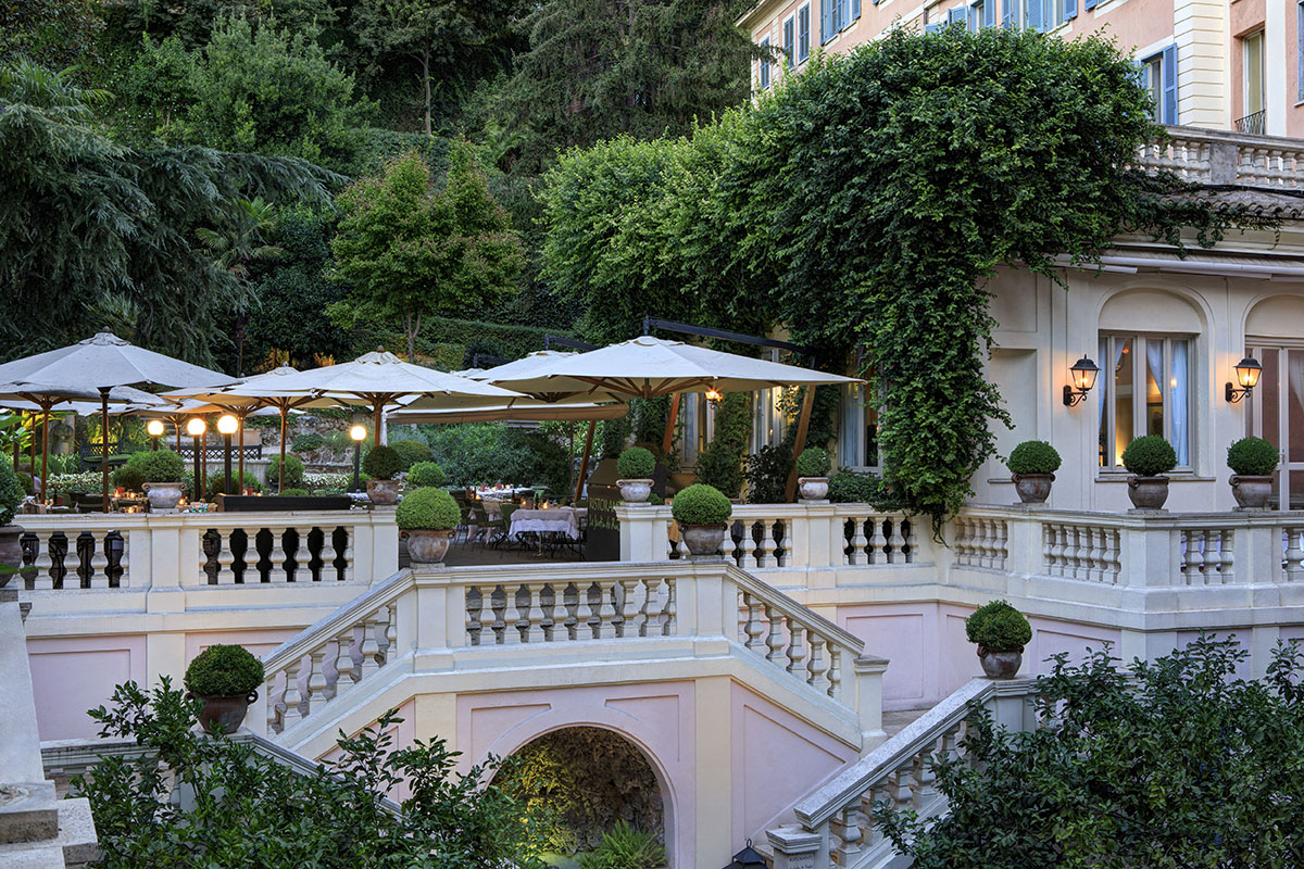 Grand terrace of a pink mansion house with umbrellas and lots of greenery