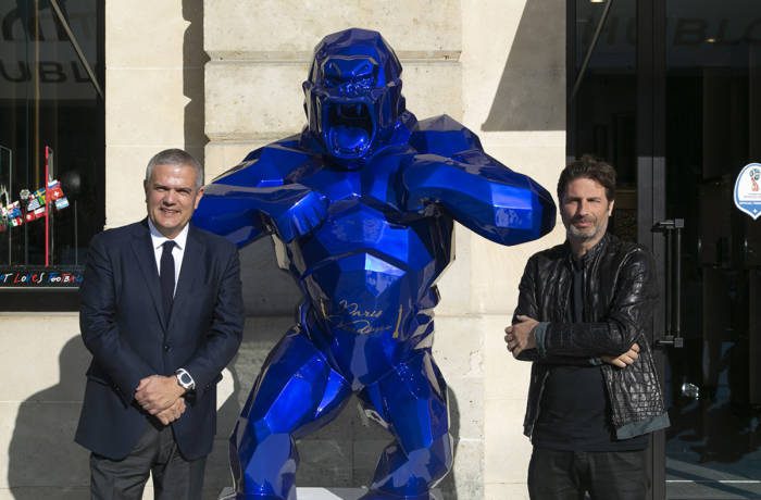 Two businessmen standing beside a giant sculpture of a blue gorilla