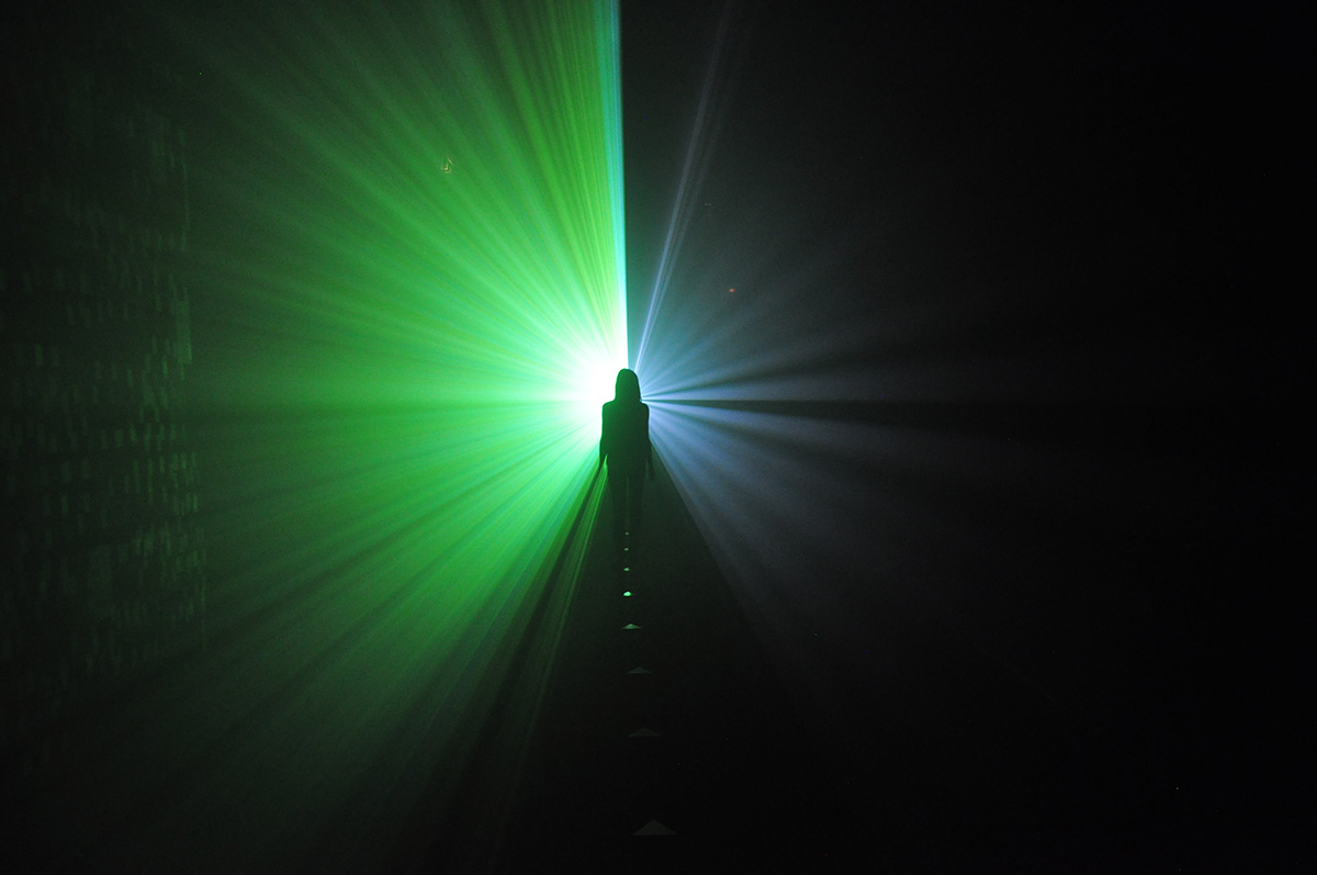 Installation image of a figure standing in a room with a bright green light