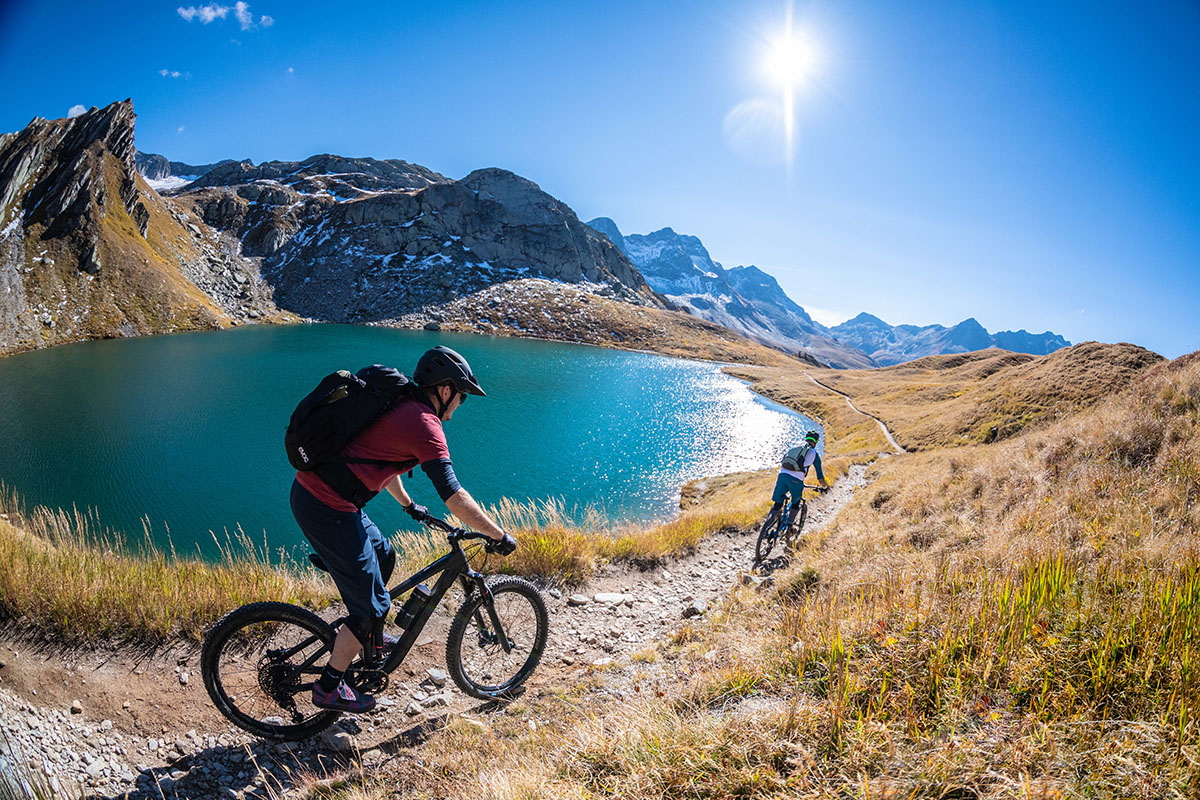 Two cyclists riding their bikes around an alpine lake in the summer