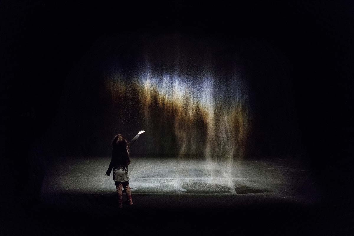 A small girl experiencing a dust art installation in a dark room