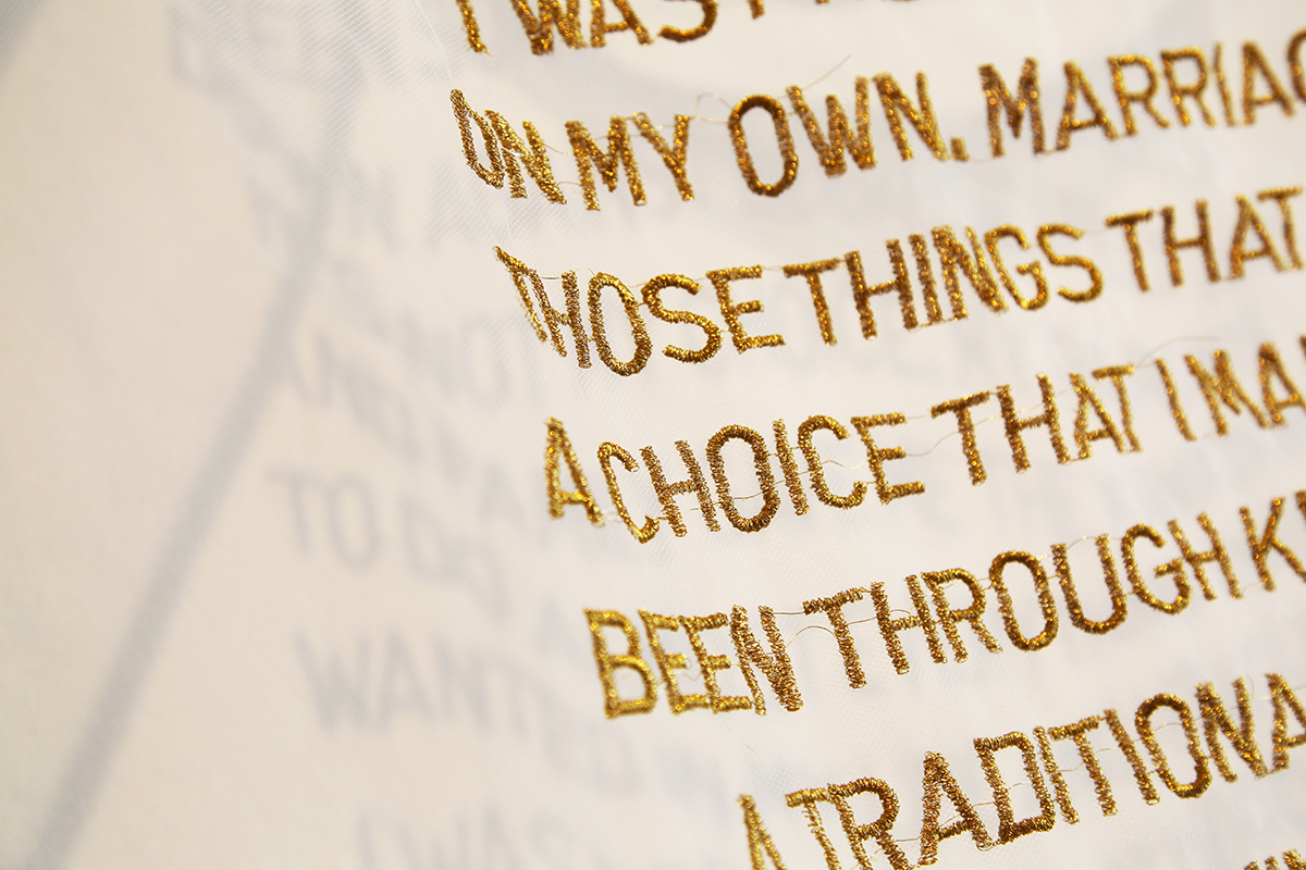 Gold embroidered words floating on a veil against a white wall